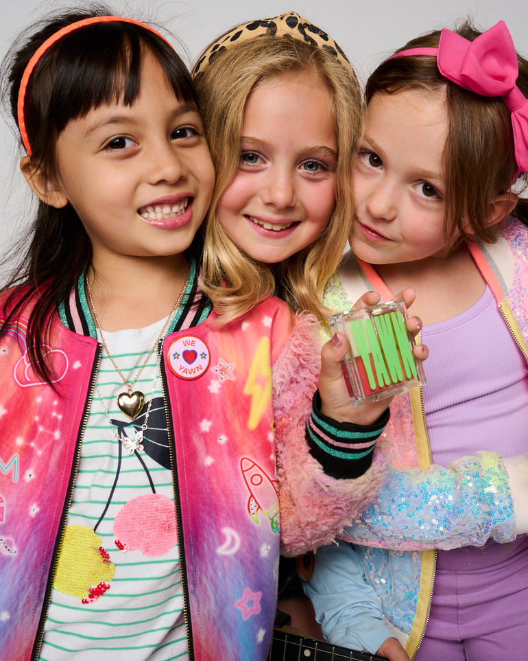 Three kids smiling for the camera, one of them holding a YAWN eyeshadow palette in their hand.