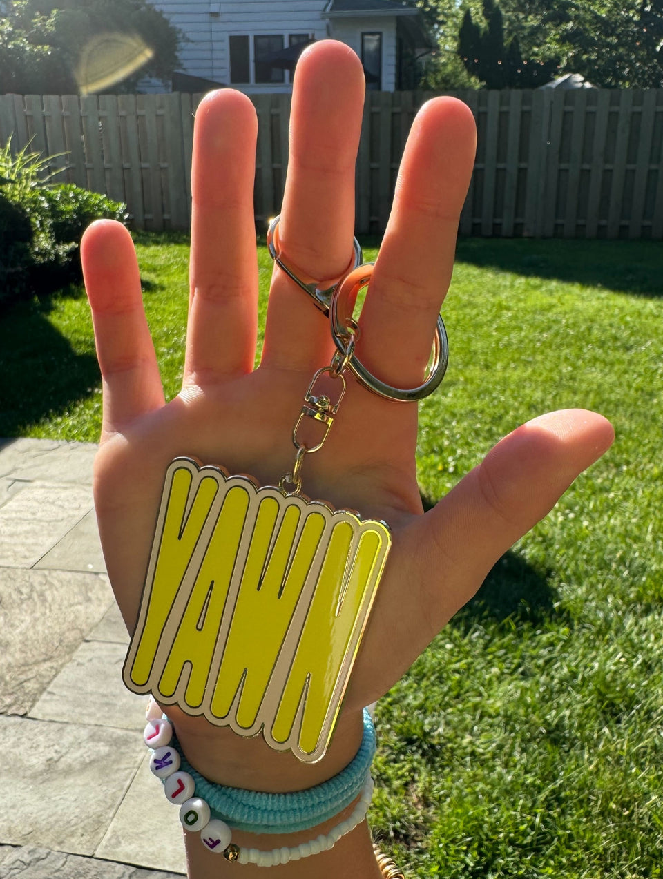 Hand holding a keychain that says YAWN in yellow with a pink border.l.