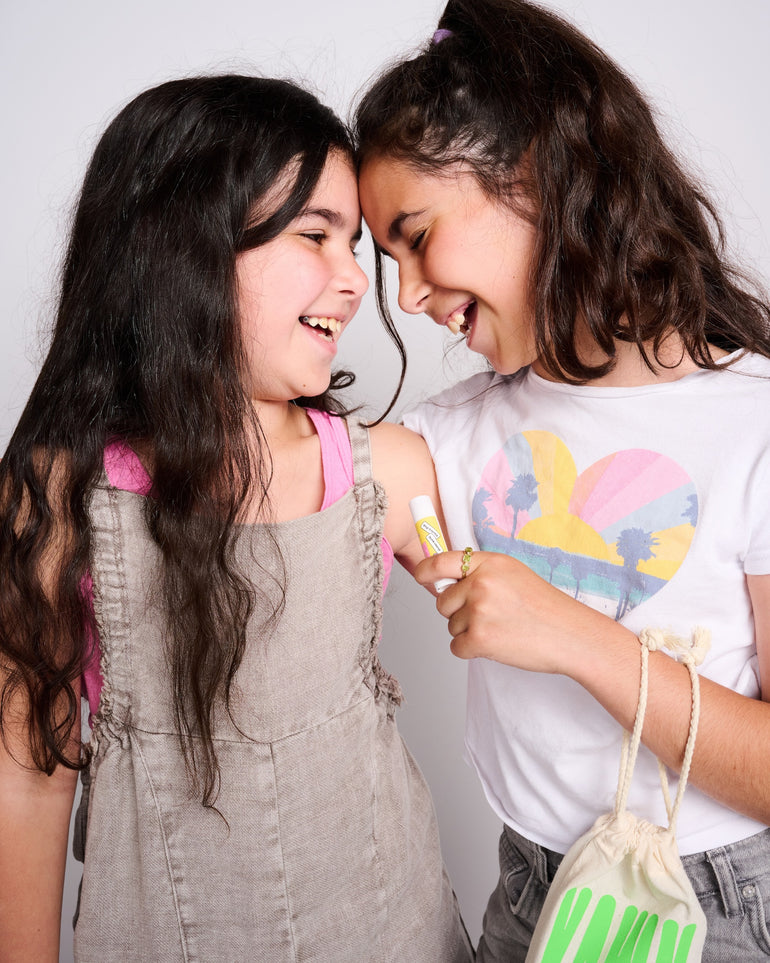 Photo of two sisters holding a YAWN lip balm and laughing with their heads touching.