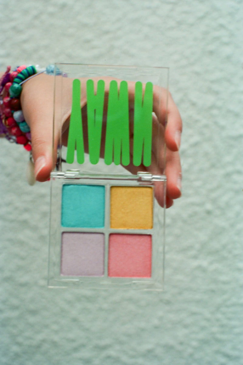 Photo of a hand holding an open YAWN  eyeshadow palette. The eyeshadow colors are bright blue, golden yellow, pink and pale purple.